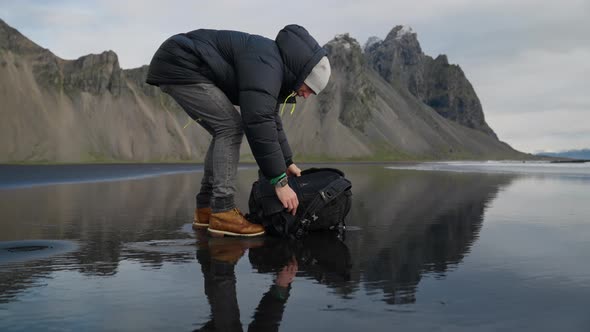 Hiker Arranging Backpack With Tripod On Wet Beach