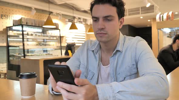 Young Man Typing Message in Cafe Browsing on Phone