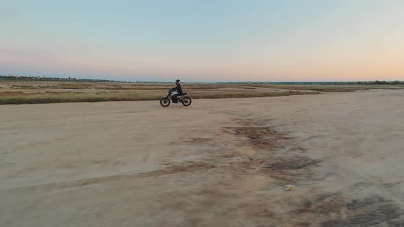 Young Stylish Woman Motorcyclist Driving Her Motorcycle in the Desert Road During Sunset