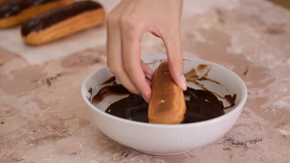 Female Hand Dips Eclair in Sweet Chocolate Close Up