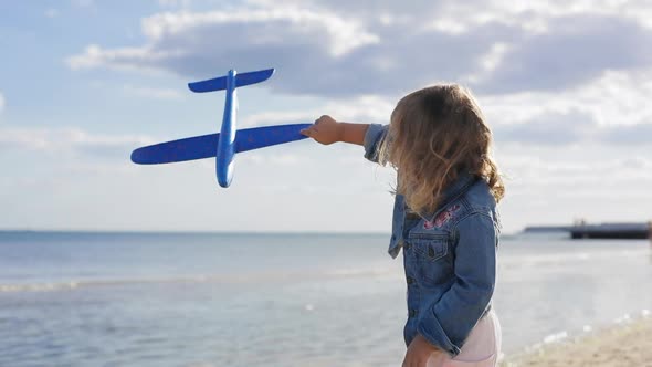 Happy Child Playing with a Toy Plane at the Beach During Summer Sunset. Girl Holds Airplane in Her