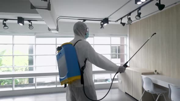 Worker in PPE suit cleaning in building with spray disinfectant water to remove covid 19