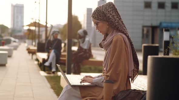 Woman Using Laptop on Bench Outdoors