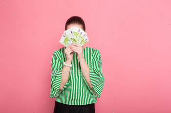  blouse and eyeglasses covering her face with fan of euro bills isolated on pink background with copyspace winning in lottery money withdraw concept.