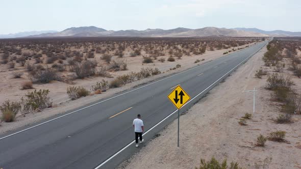 A man walking on a highway in the desert.