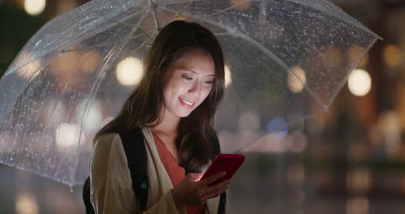 Woman use of mobile phone and hold with umbrella in the evening