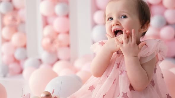 A Cute Little Girl in a Dress Sits Near a Birthday Cake with the Number 1