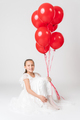 Smiling girl in white dress holding lot of red balloons in hand looking at camera with happy emotion - PhotoDune Item for Sale