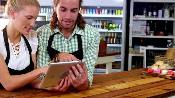 Smiling waiter and waitress standing at counter using digital