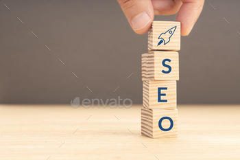 lding a wooden block with rocket icon and SEO word. Copy space