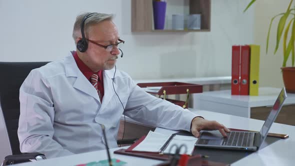 Old doctor in medical office working online. 