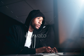 No code is uncrackable. Low angle shot of a young male hacker cracking a computer code in the dark.
