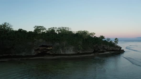 Title reveal shot over rocky peninsula on coast of Fiji during dawn, aerial