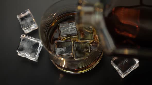 Pouring Whiskey, Cognac Into Glass with Ice Cubes. Pour of Alcohol Drink