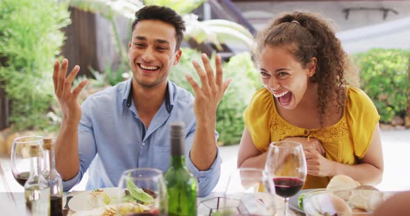 Diverse couple laughing with friends at dinner party on patio