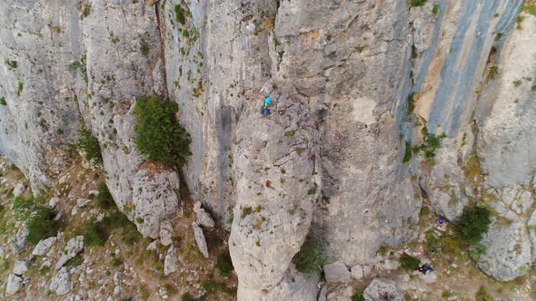 Aerial view of man climbing a stone mountain with safe equipment.