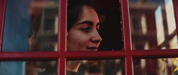 Smiley young woman in a phone booth searching for somebody while talking by phone