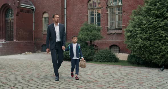 Handsome Dad Businessman and Litlle Child with Bag Talking While Holding Hand in Hand. Man with His