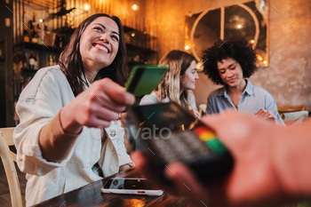 Happy young woman paying bill with a contactless credit card in a restaurant. Female smiling holding