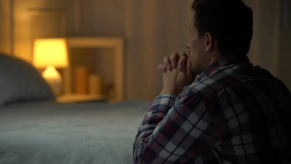 Religious Young Man Praying in Evening Near Bed