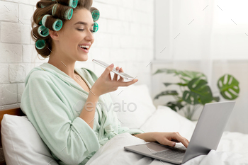 Woman Using Voice Search App On Cellphone And Laptop Indoor