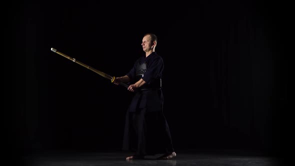 Masculine Kendo Warrior Practicing Martial Art with the Bamboo Bokken on Black Background.