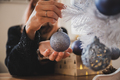 Closeup view of female hands about to hang a shiny blue holiday bauble on white christmas tree - PhotoDune Item for Sale