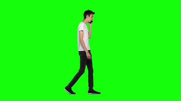 Tall Skinny Teen Guy Calmly Walking and Talking on Mobile Phone on Green Screen. Chroma Key. Profile