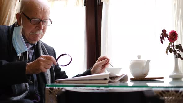 Retired Senior Man with Gray Mustache Reads Newspaper at Home in the Kitchen