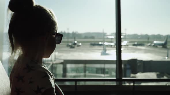 Child Girl in Sunglasses Waiting for a Plane at Sunset Sits at Airport Passenger Terminal Waiting