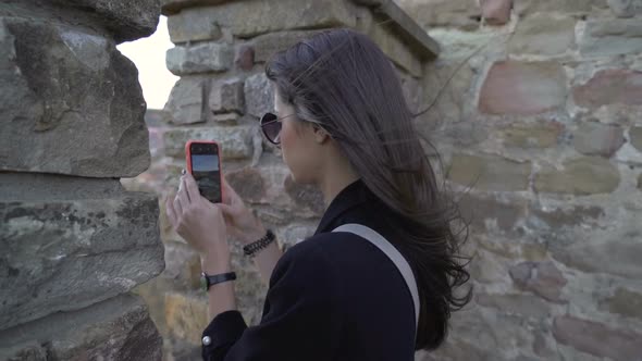 Tourist Girl Watching Trough Medieval Fortress Wall and Taking Pictures of the Panoramic View