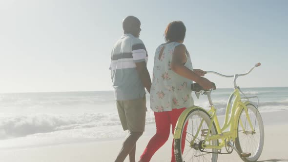 Senior african american couple walking with bicycle on sunny beach