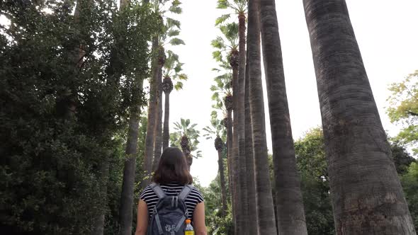 Following slowmotion shot of a young asian woman who walks under palmtrees in Athen.