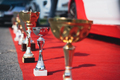 close up perspective view of golden and silver trophy on red carpet with cars in the background - PhotoDune Item for Sale