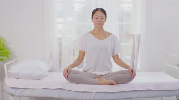 Calm of wellness Asian young woman sit on bed breathing with yoga lotus pose