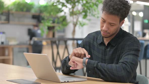 African American Man with Laptop Checking Smart Watch