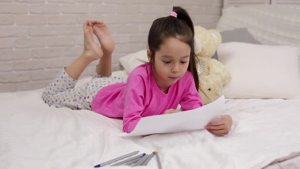 Cute Little Girl Drawing Pictures While Lying on Bed