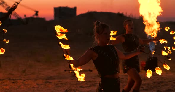 A Man in a Raincoat with Two Flamethrowers Lets Out a Fiery Flame Standing at Sunset on the Sand