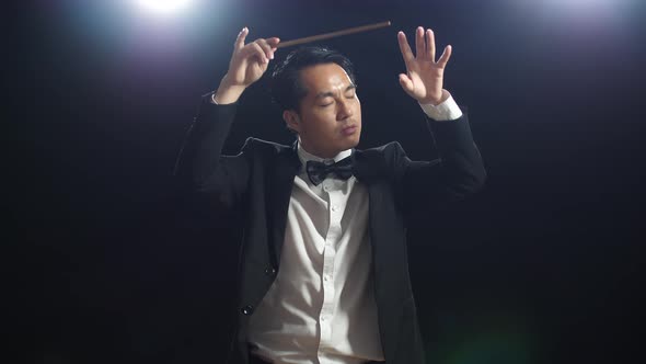 Asian Conductor Man Holding A Baton Closing His Eyes And Showing Gesture In The Black Studio