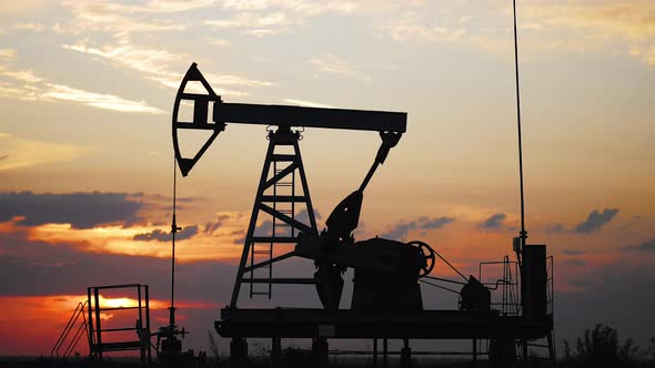 Silhouette Working Oil Pump in Deserted District at Sunset