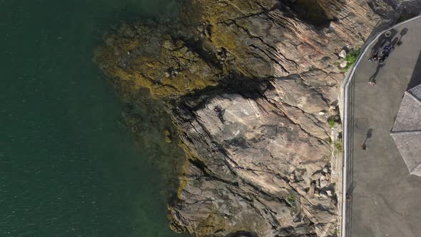 a top down view of a man laying on rocks by the water on a sunny day. The camera boom up to show peo