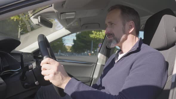 A Middleaged Caucasian Man Picks Up a Call on a Smartphone and Talks Via Bluetooth in His Car