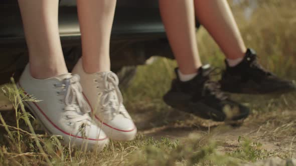 Women's Legs in Sneakers Dangling From Car Trunk