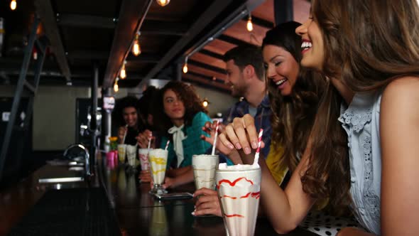 Smiling friends having smoothie with straw