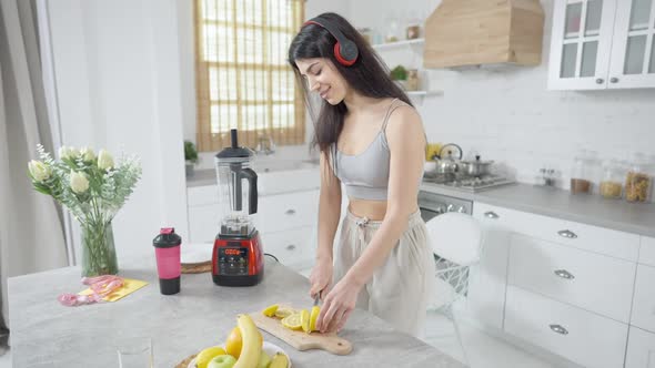 Young Middle Eastern Woman in Headphones Dancing in Kitchen Slicing and Eating Lemon