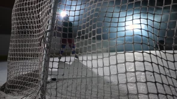 A View Behind the Net of Hockey Forward Who Hits the Puck with His Stick and Scores a Goal