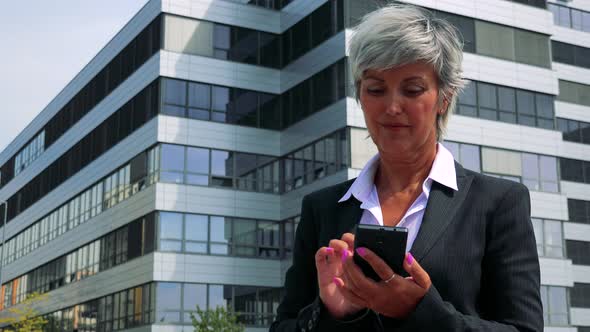 Business Middle Age Woman Works on the Smartphone - Company Building in the Background