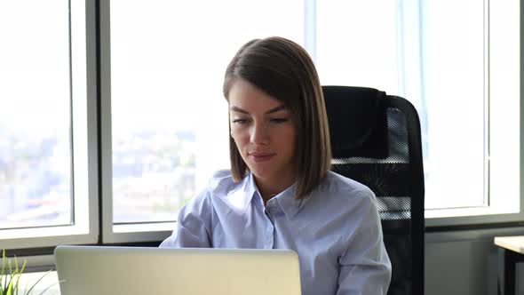 Happy young businesswoman is analizing financial documents on laptop at office