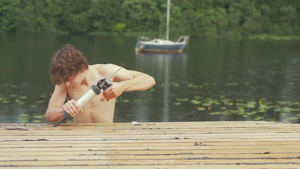 Young carpenter using sealant gun to seal cabin roof planking old wooden boat maintenance.