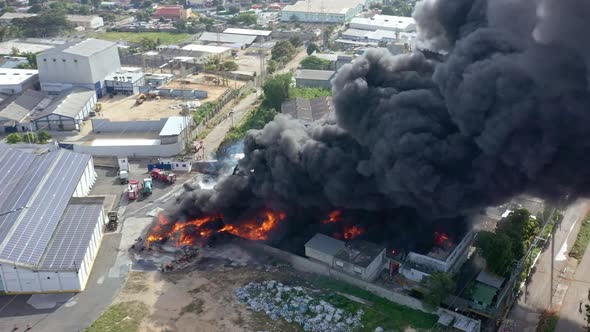 Aerial drone shot over black smoke column of burning warehouse